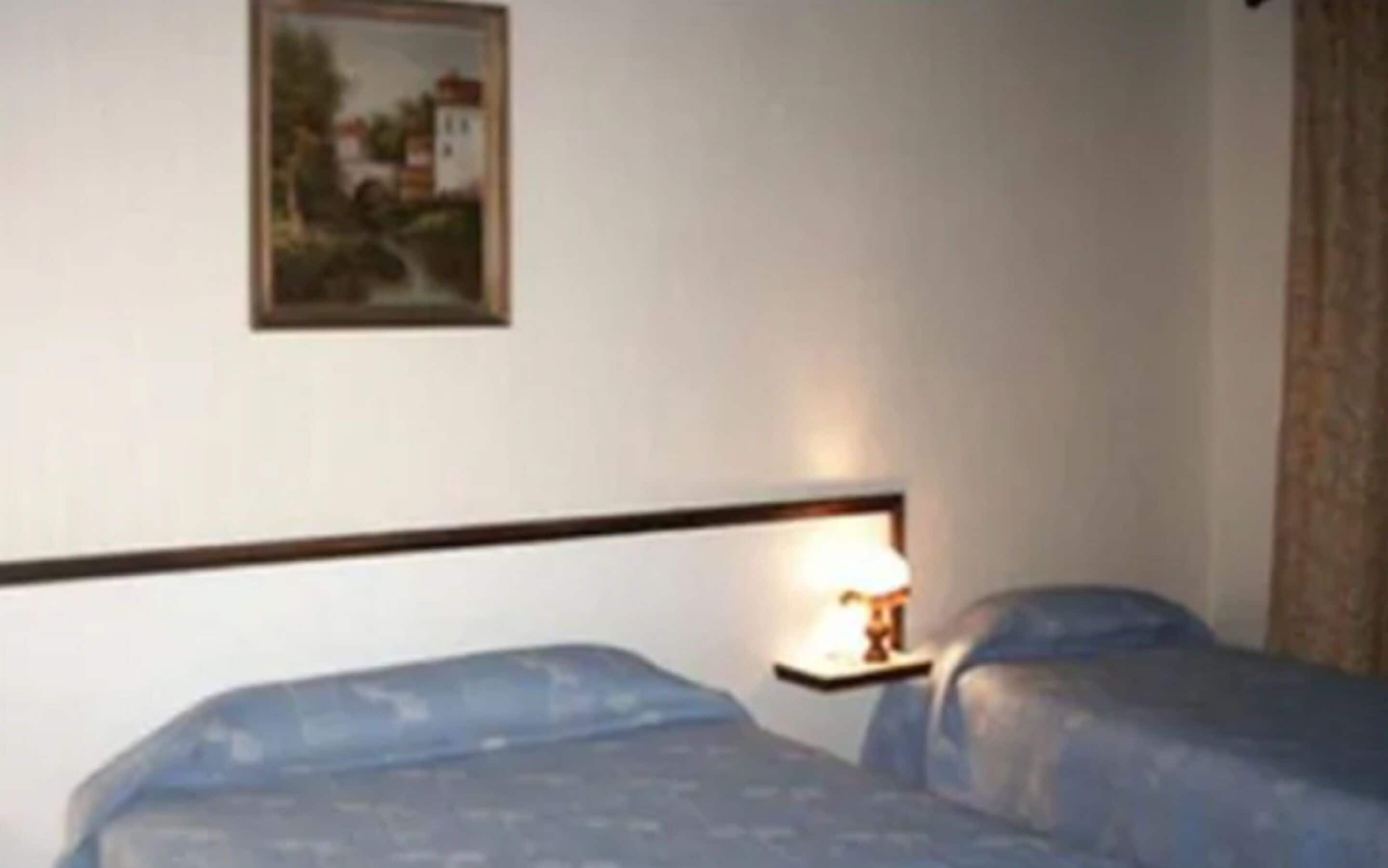 Una habitación de hotel con dos camas, una mesita de noche con lámpara y un cuadro enmarcado en la pared.
