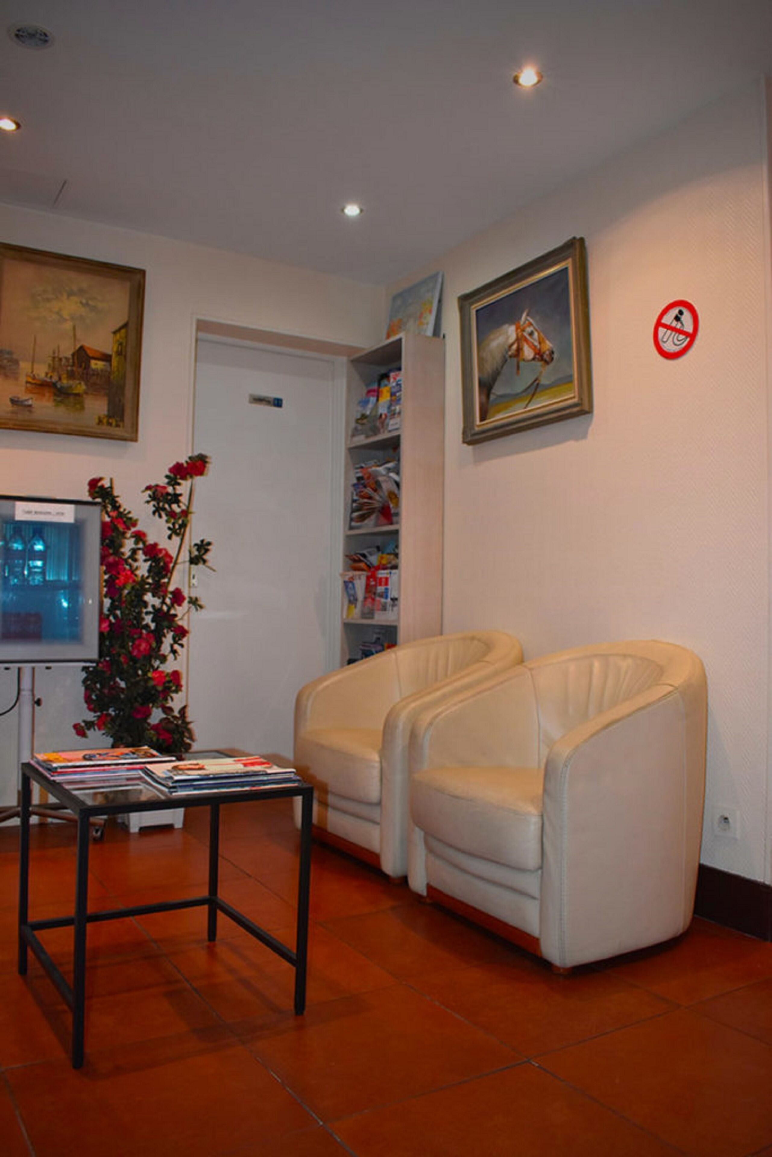 A room with a white door, a television, a bookshelf, a small table with magazines, and two white leather chairs.