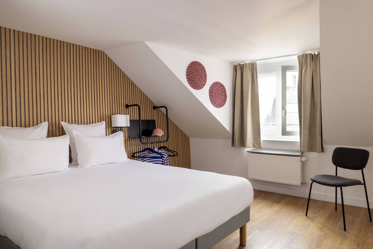 A bedroom with a bed, a chair, a radiator, and a window with curtains.