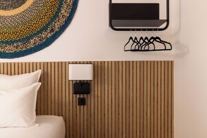 Habitación de hotel con cama, televisor y lámpara fijados a la pared, y un panel de pared de madera.