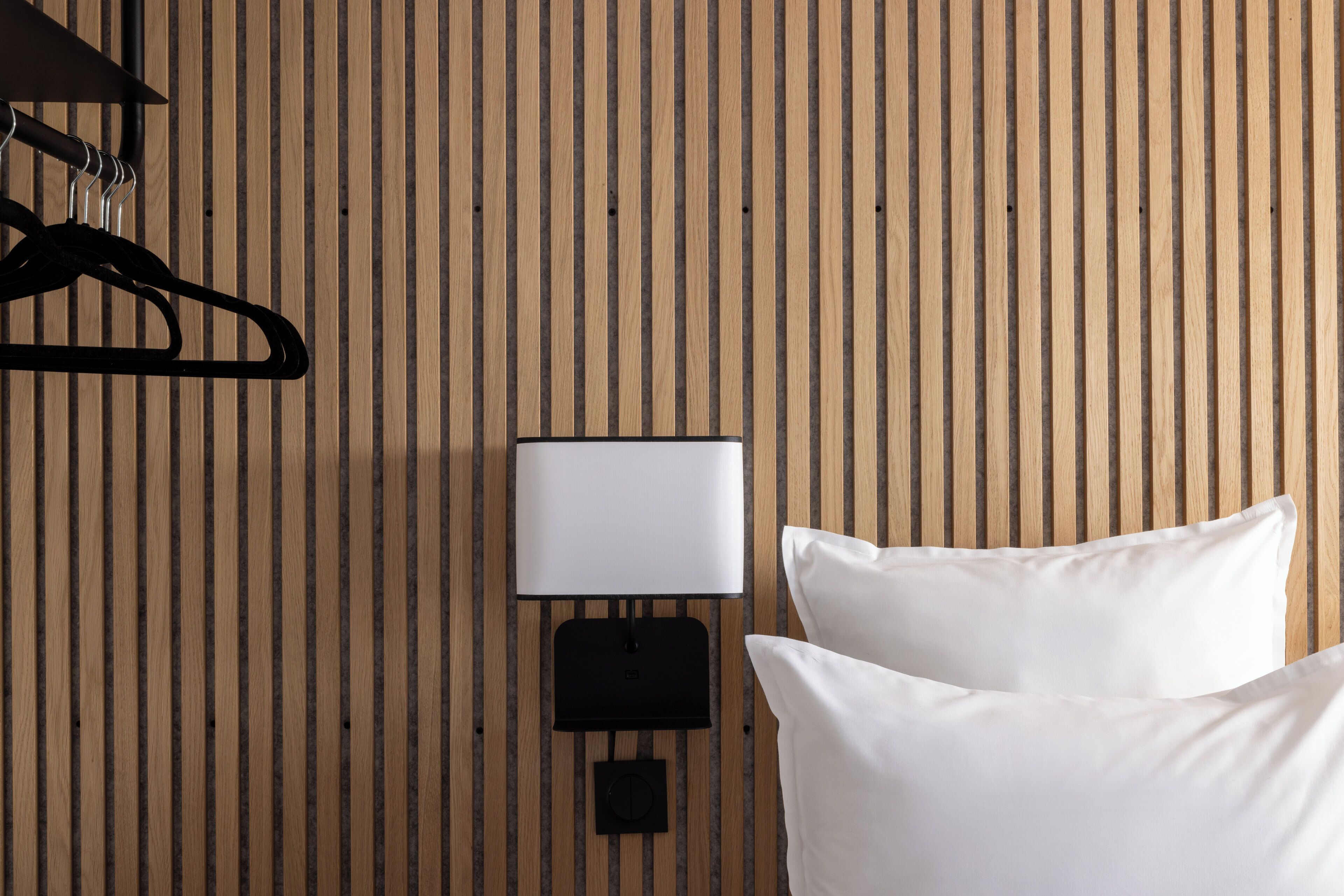 A room with a wooden slat wall, a black wall-mounted lamp, and two white pillows.