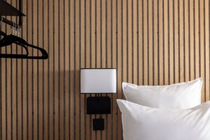 A room with a wooden slat wall, a black wall-mounted lamp, and two white pillows.
