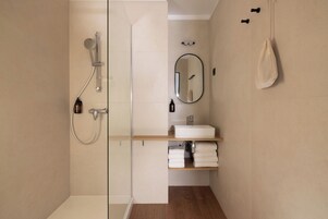 Un baño moderno con cabina de ducha de vidrio, un lavamanos blanco con espejo y un perchero en la pared.