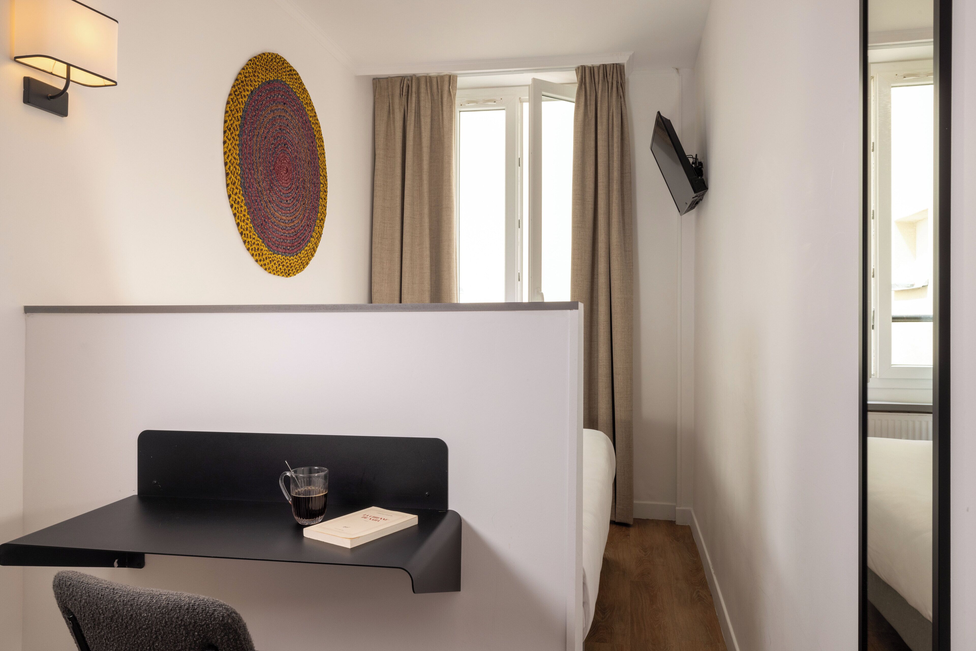 A hotel room with a desk, chair, and a large window with curtains.