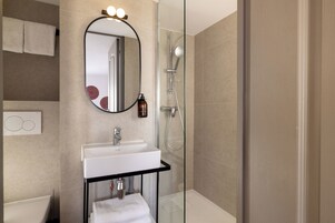 A modern bathroom with a glass-enclosed shower, a white sink, and a mirror with lights.