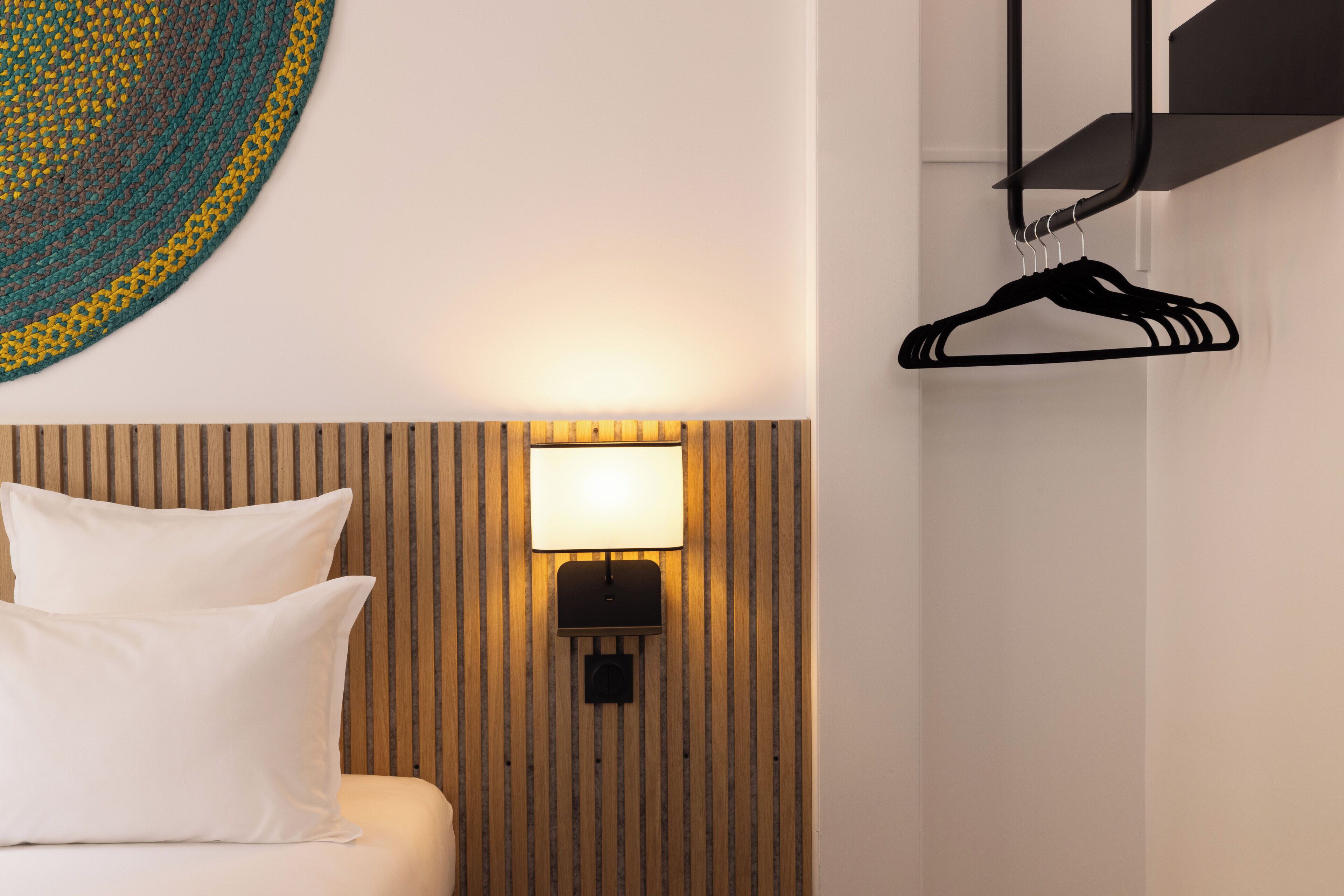 Una habitación de hotel con una cama, una lámpara de pared y un perchero.