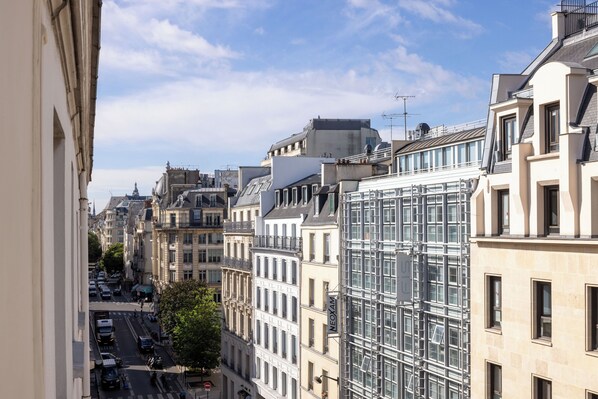 A city street with historic buildings, a modern glass structure, and a clear sky.