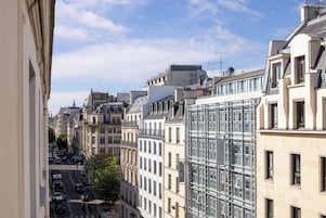 A city street with historic buildings, a modern glass structure, and a clear sky.