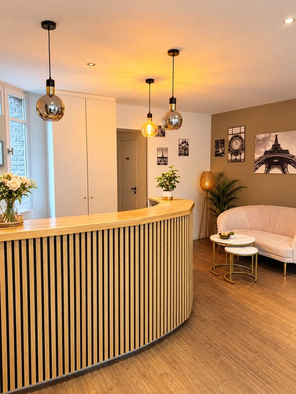 A modern reception area with a wooden reception desk, pendant lighting, a sofa, and wall art including a depiction of the Eiffel Tower. - Hotel Douglas (Puteaux)