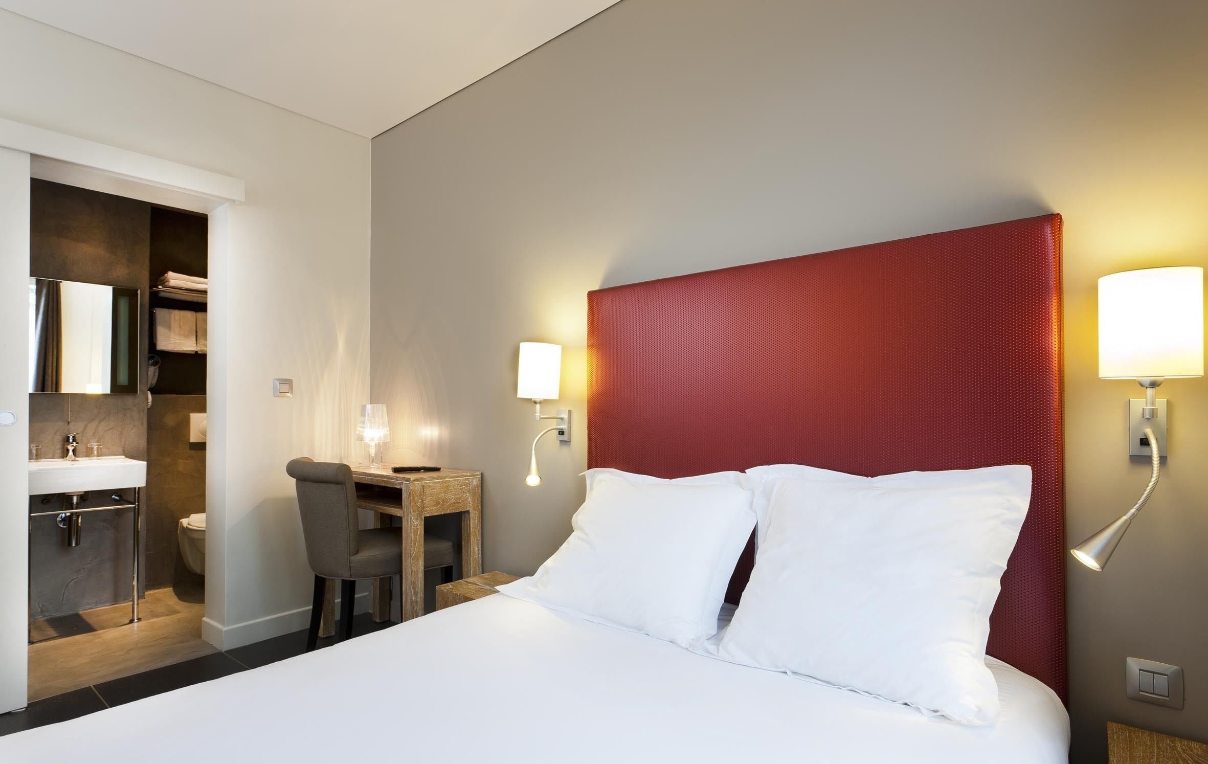 Une chambre d’hôtel équipée d’un lit, d’un bureau, d’une chaise, d’une salle de bain et de deux lampes fixées au mur.