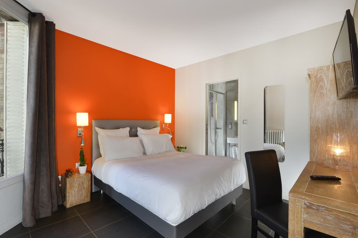 A modern hotel room with a large bed, two bedside lamps, a desk with a chair, and a TV.