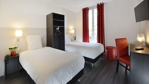 Une chambre d’hôtel avec deux lits, un bureau avec une chaise, une télévision et un rideau rouge.
