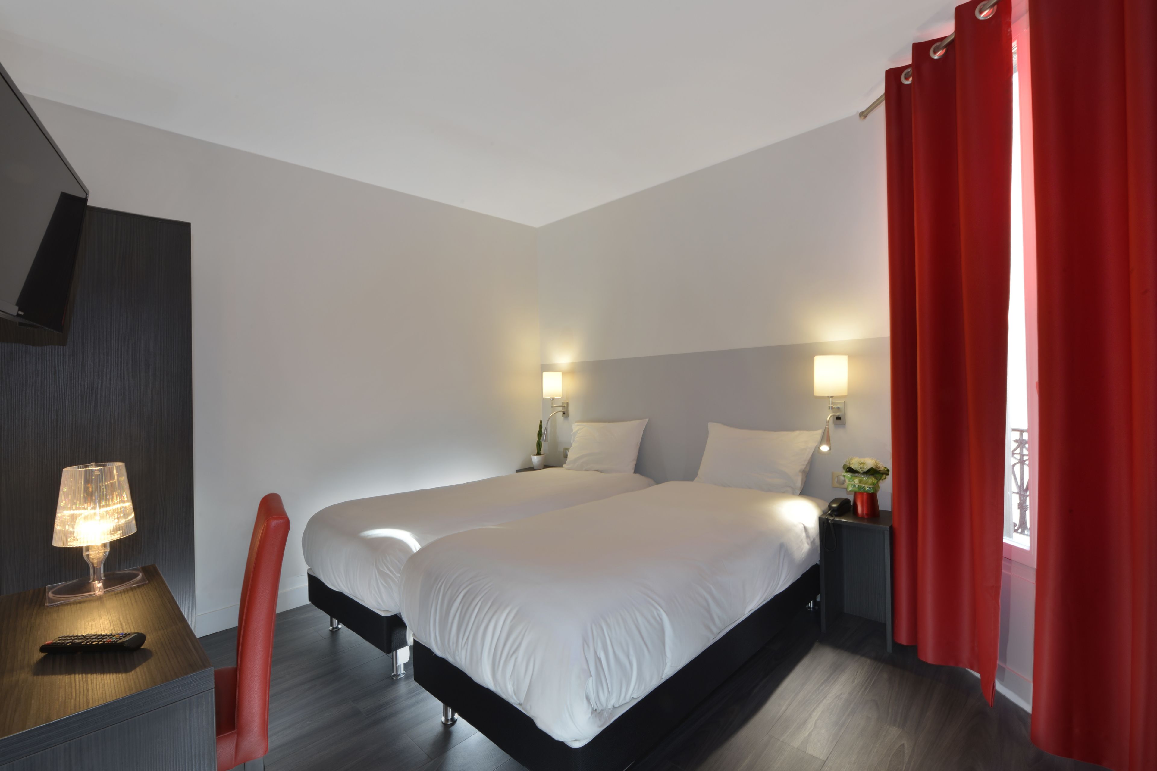 Habitación de hotel con dos camas, un escritorio con lámpara, una silla y una mesita de noche con teléfono y planta.