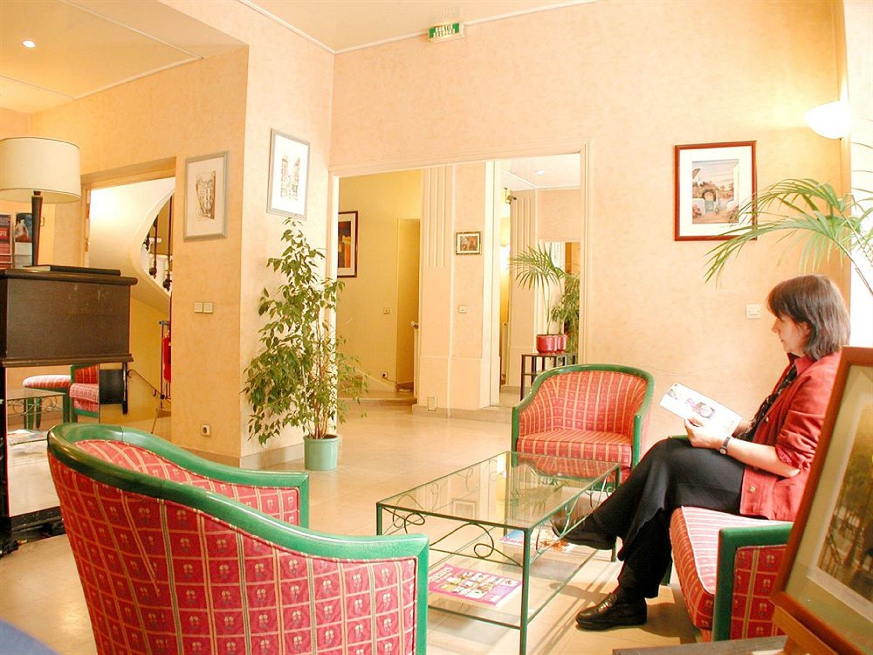 A lobby with red patterned chairs, a glass coffee table, and a person reading a magazine.