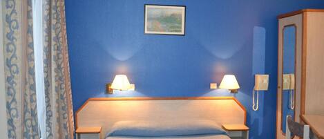 A hotel room with a bed, two bedside lamps, a telephone, a mirror, and a painting on the wall.