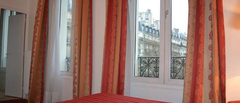 Quarto de hotel com uma cama, uma janela com cortinas e vista para edifícios.