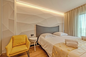 A modern hotel room with a geometric wall design, a bed with a patterned bedspread, a yellow armchair, and a small round table.