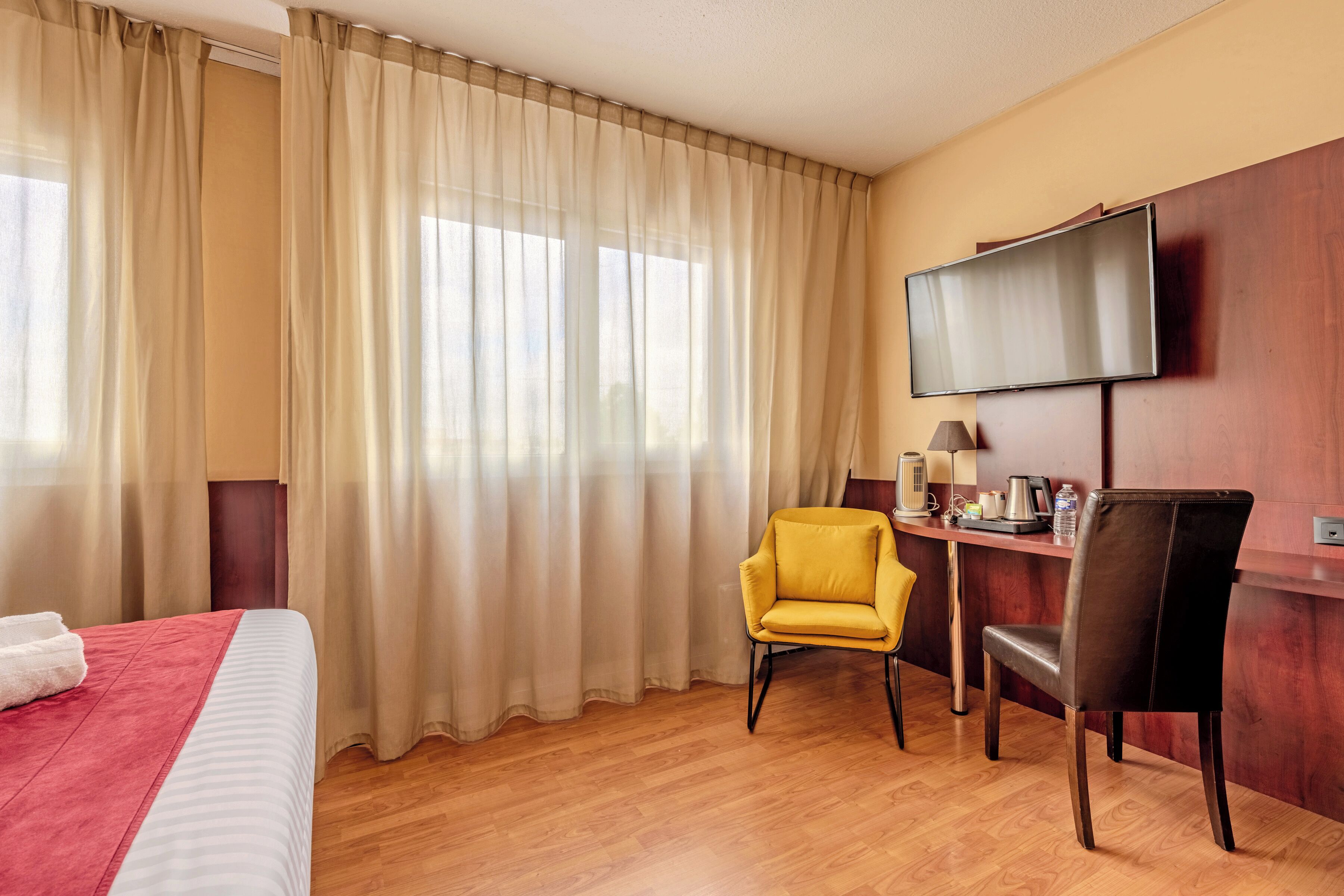 A hotel room with a bed, a desk with a chair, a television, and a window with curtains.