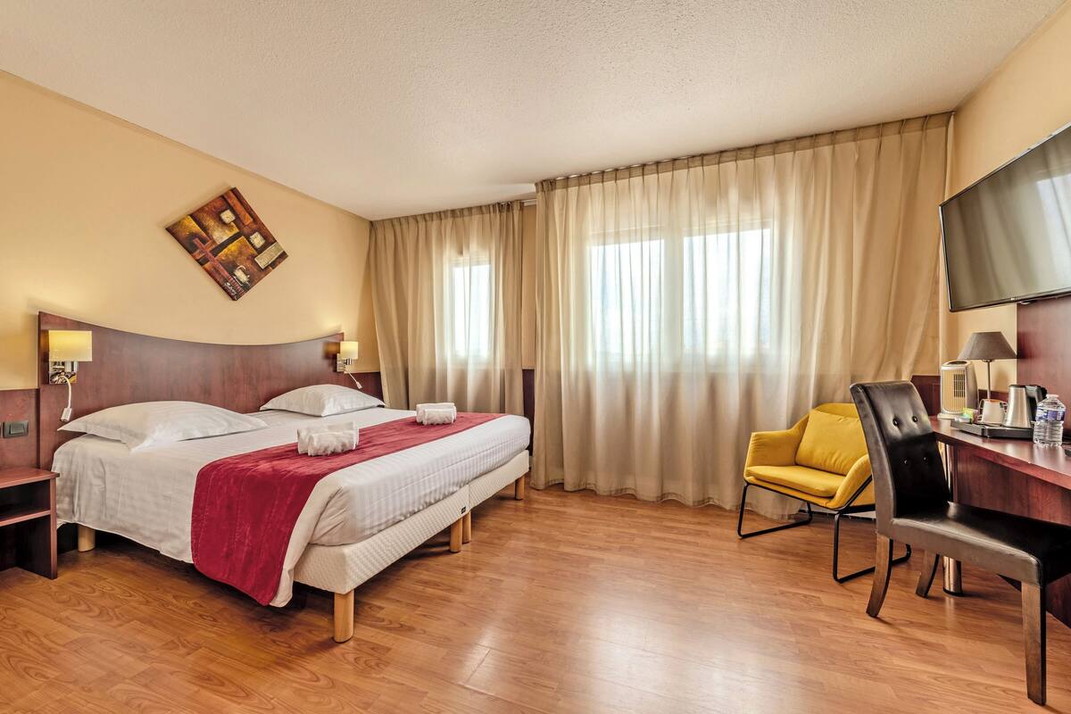A hotel room with a bed, a desk, a chair, a television, and a window with curtains.