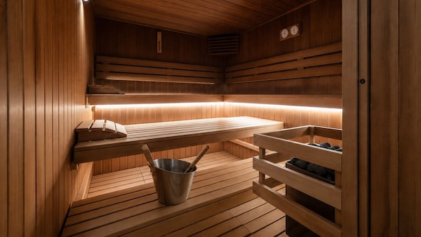 A sauna with wooden benches, a bench with a bucket, and a wall-mounted heater.