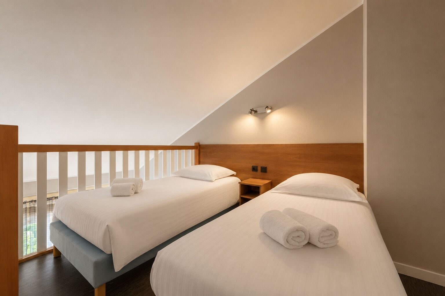 Quarto de hotel com duas camas, uma cabeceira de madeira, uma mesa de cabeceira e uma varanda com guarda-corpo.