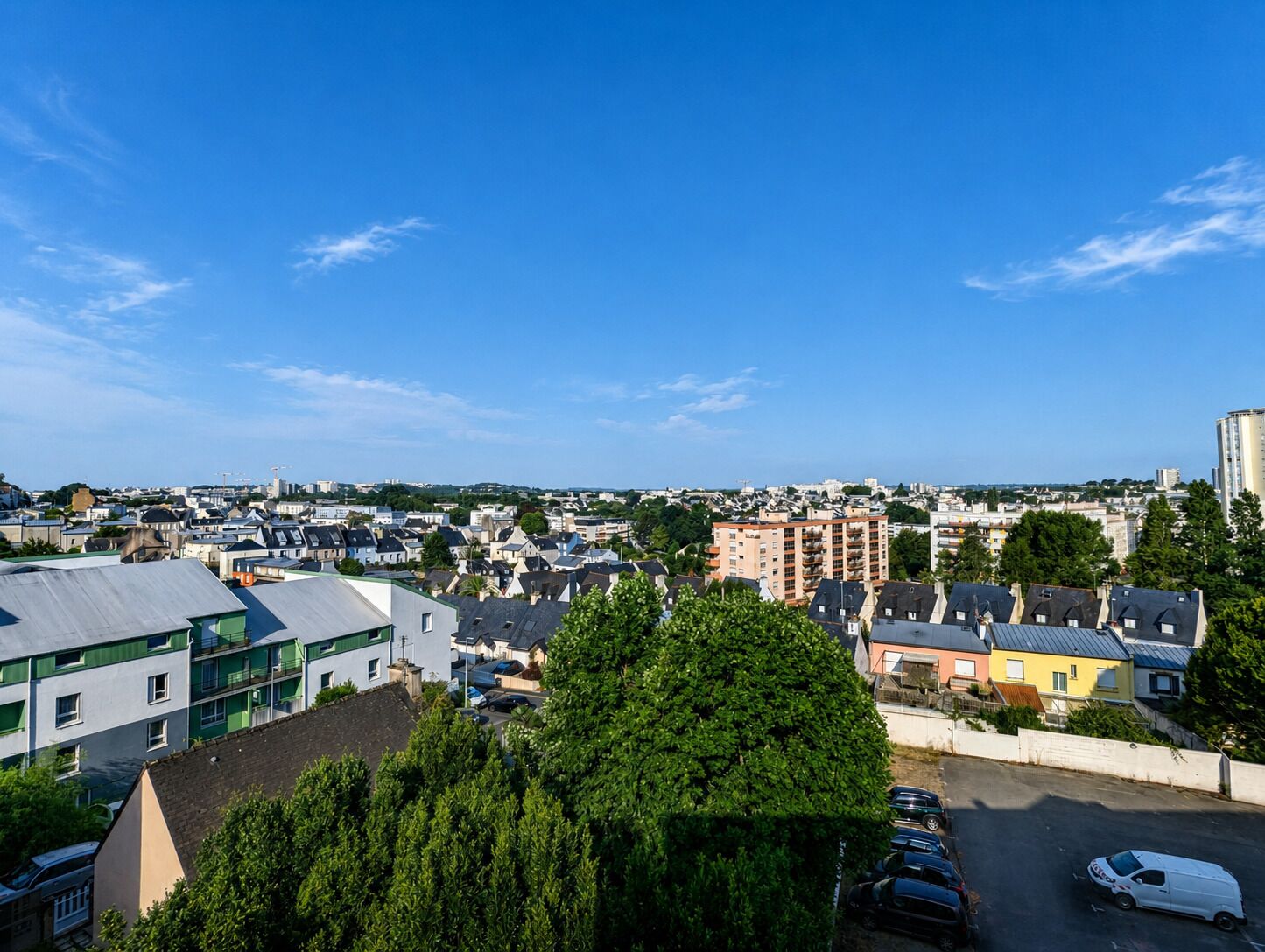 A residential area with a mix of houses and apartment buildings, a parking lot, and a clear blue sky.