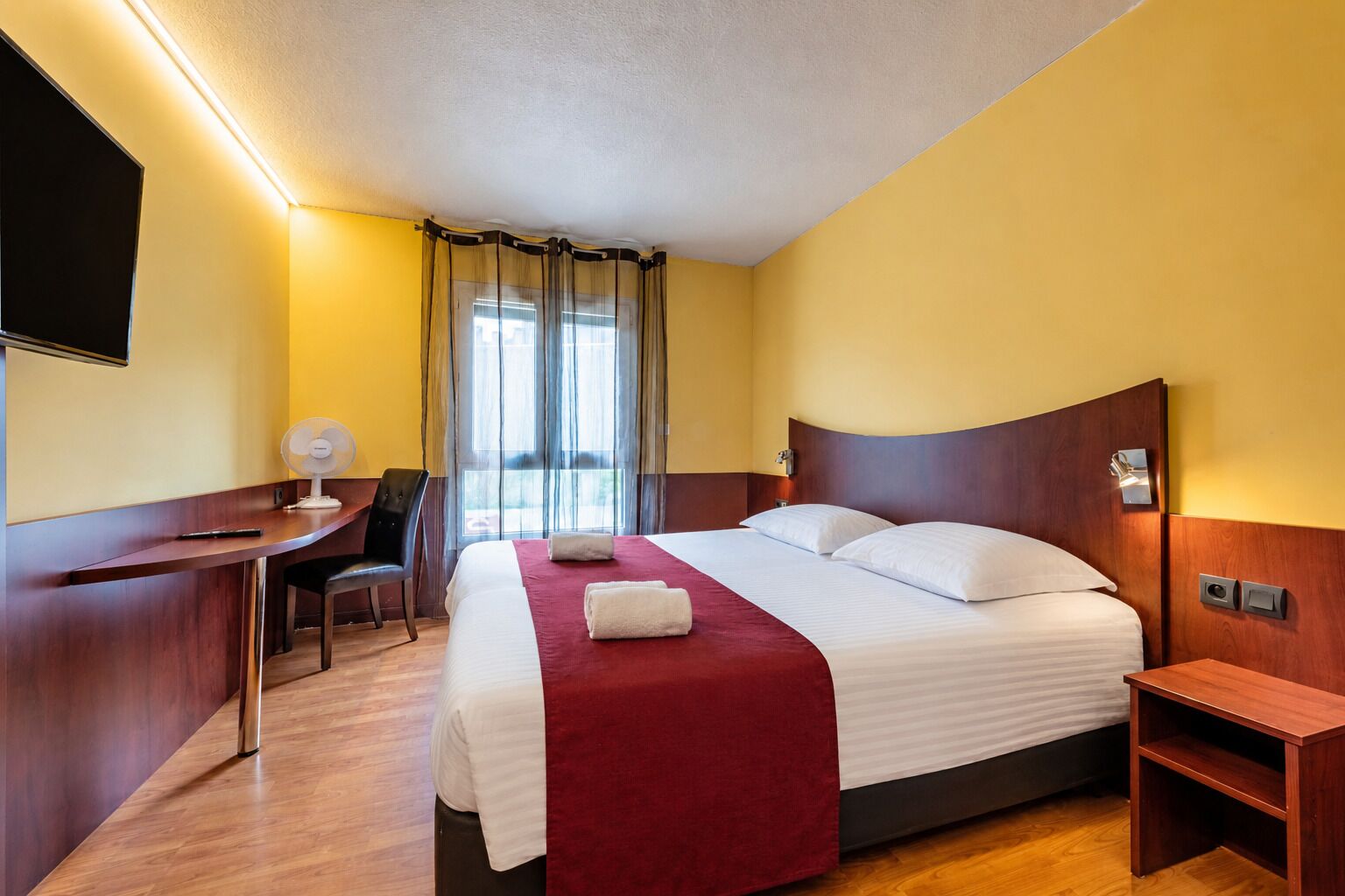 A hotel room with a bed, a desk, a chair, and a TV.