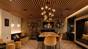 A modern interior with a wooden ceiling, a central dining table with chairs, a sofa, and a TV displaying a fire.
