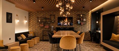 Un intérieur moderne avec un plafond en bois, une table à manger centrale entourée de chaises, un canapé et un téléviseur diffusant une image de feu de cheminée.