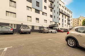 Um estacionamento com vários carros, um edifício de hotel com varandas e um céu claro.
