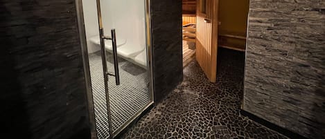 Un baño moderno con cabina de ducha de vidrio, puerta de madera y suelo de baldosas.