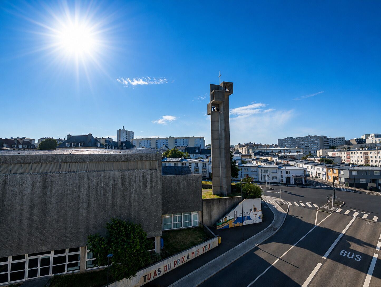 A cityscape with a prominent concrete tower, a clear blue sky, and a road with a bus lane.