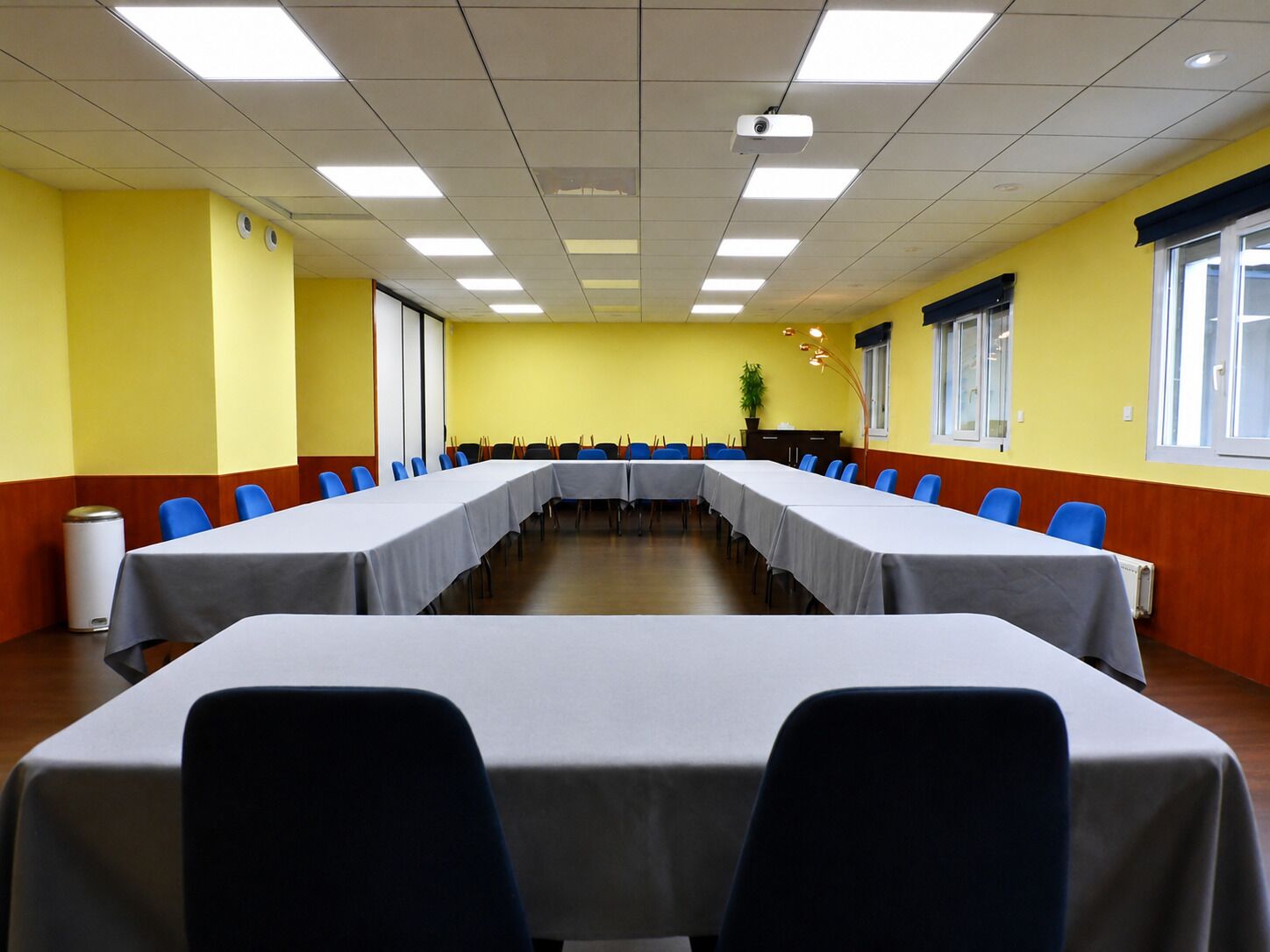 Ein Konferenzraum mit einem langen Tisch, blauen Stühlen, gelben Wänden und einem Projektor.