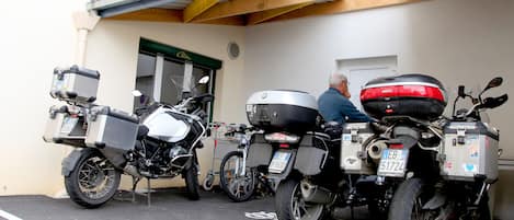 Three motorcycles parked in a covered parking area with a building entrance in the background.