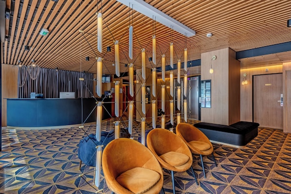 Um hall com piso estampado em padrão geométrico, um balcão de recepção e assentos modernos.
