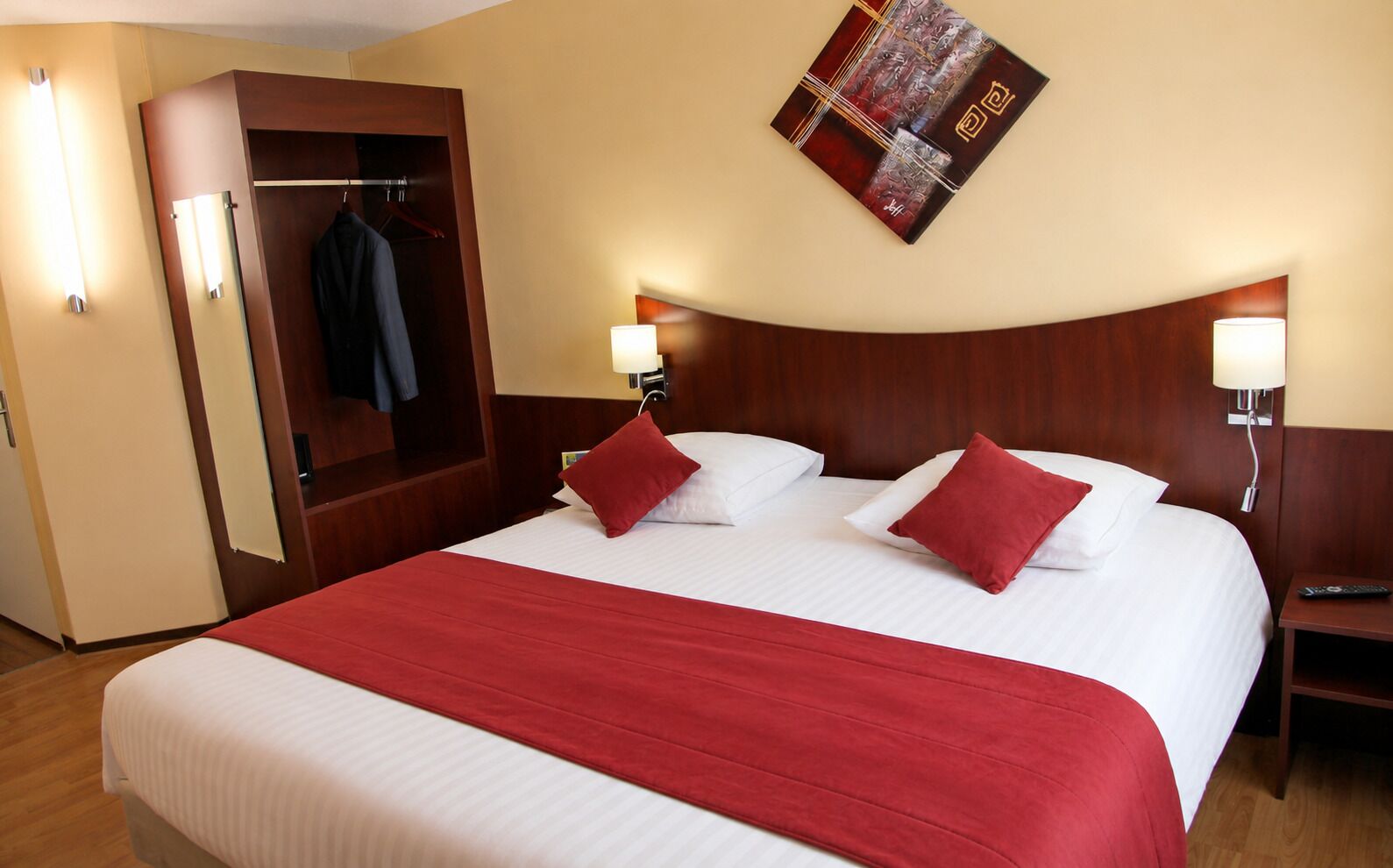 Habitación de hotel con una cama grande, dos mesitas de noche, un armario y una obra de arte en la pared.