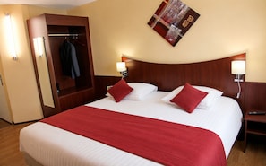 A hotel room with a large bed, two bedside tables, a wardrobe, and a wall-mounted artwork.