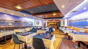 Een restaurant met tafels gedekt voor diners, uitzicht op zee en een scheepswiel aan de muur.