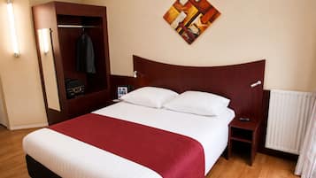 A hotel room with a bed, a nightstand, a coat rack, and a painting on the wall.