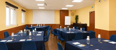 A conference room with multiple tables, chairs, a projector screen, and a whiteboard.