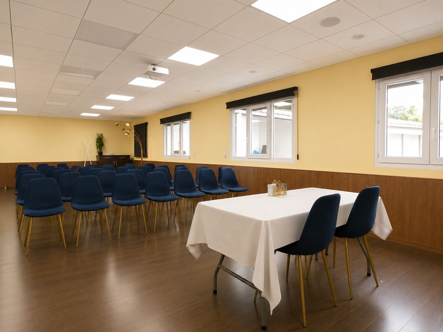 A conference room with rows of chairs, a table with a white tablecloth, and windows with blinds.
