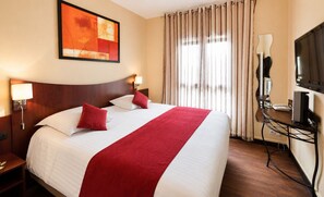 A hotel room with a large bed, a desk with a computer, a TV, and a painting on the wall.