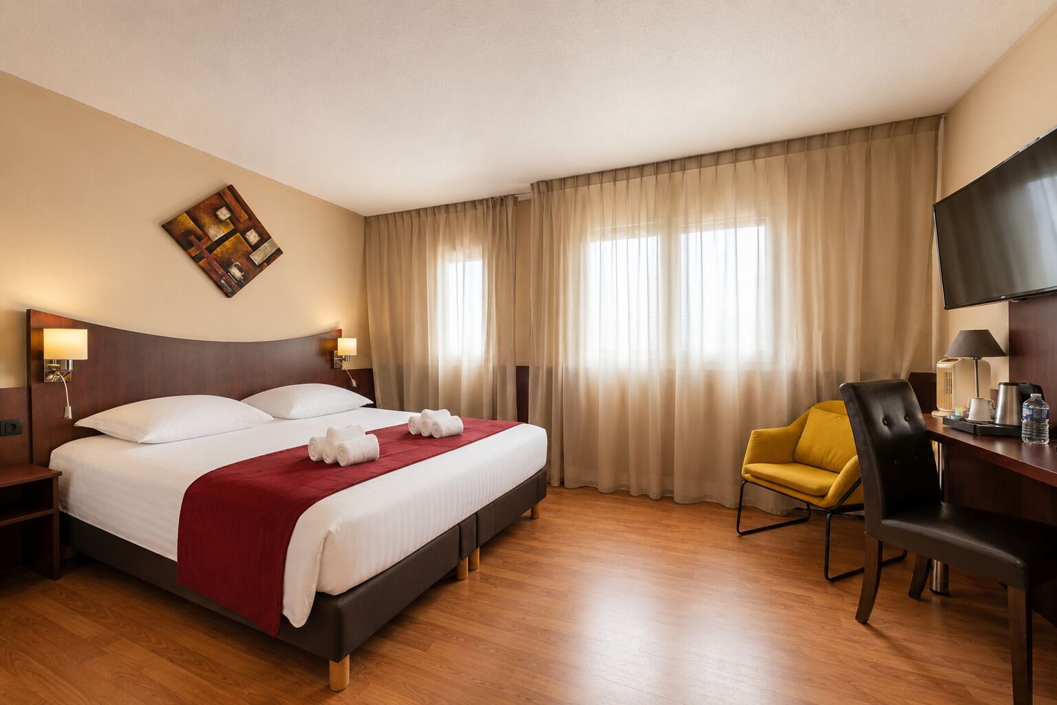 A hotel room with a large bed, a desk with a chair, a TV, and a painting on the wall.