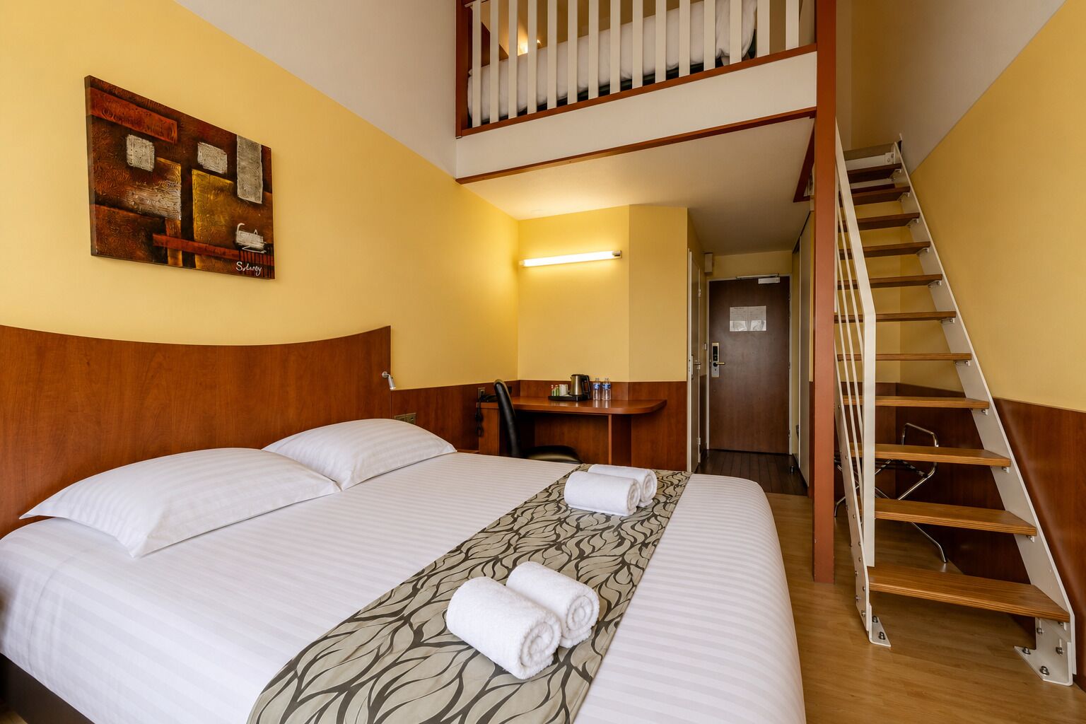 Une chambre d’hôtel avec un grand lit, un bureau, une chaise, un escalier et un tableau au mur.