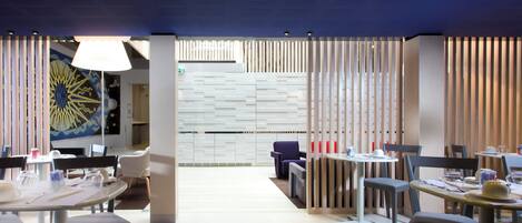A modern dining area with round tables and chairs, a decorative wall with a sun design, and a ceiling with recessed lighting.