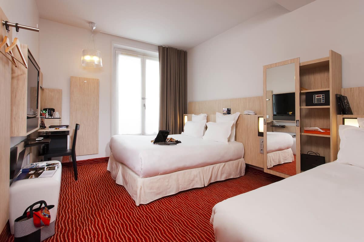 Una habitación de hotel con cama, escritorio, silla, armario y un amplio ventanal.