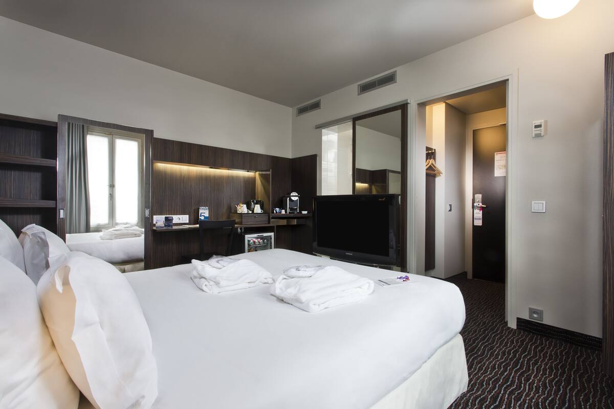 Una habitación de hotel con una cama grande, televisión de pantalla plana, minibar, escritorio y espejo.