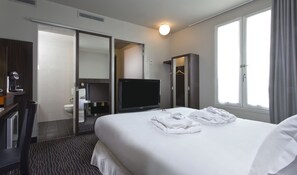 Ein Hotelzimmer mit Bett, Fernseher, Schreibtisch mit Kaffeemaschine, Kleiderschrank und angrenzendem Badezimmer.