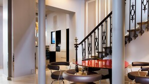 Un interior moderno con una escalera, una zona de comedor con mesas y sillas redondas, y una cocina a la vista.