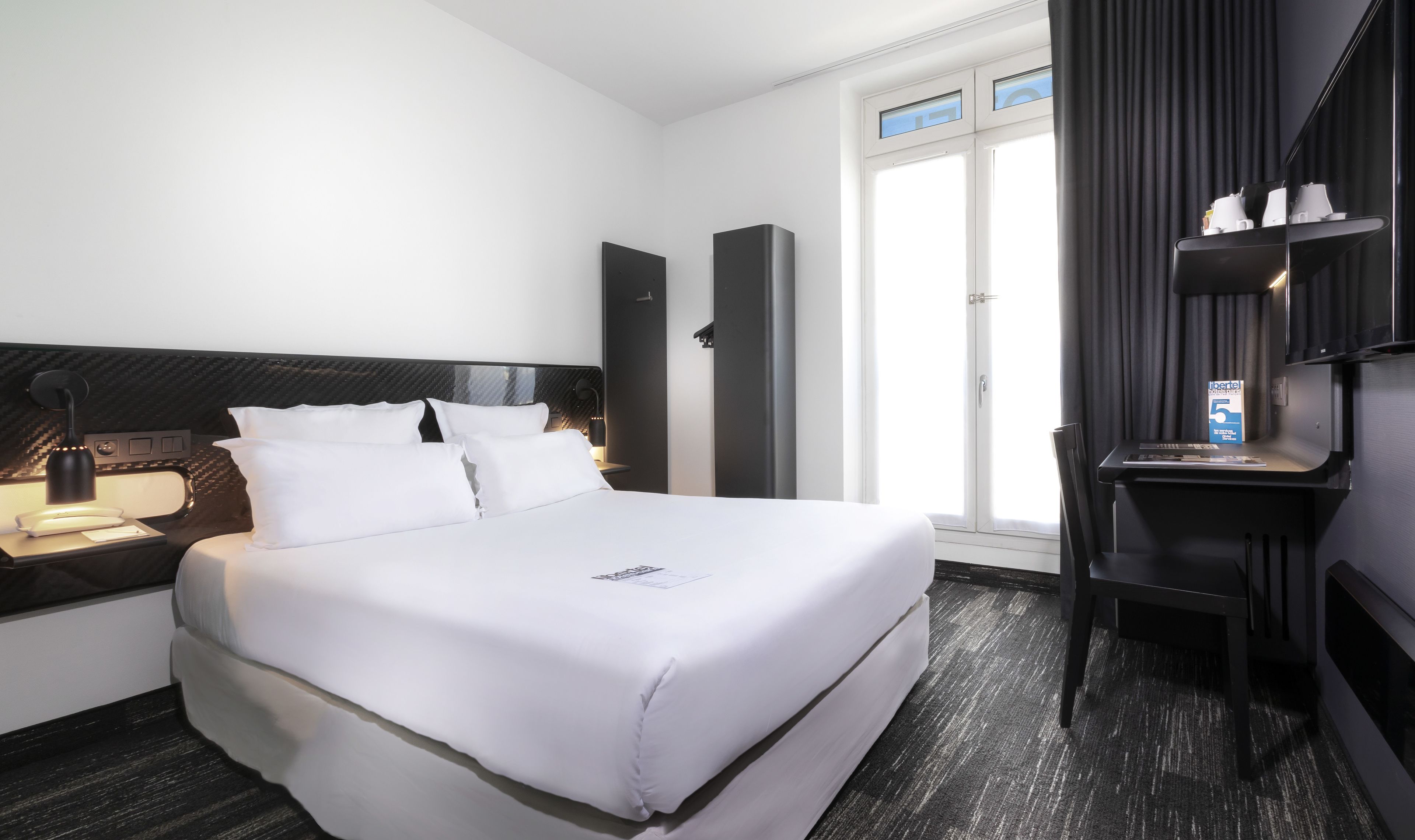 A modern hotel room with a large bed, a desk, and a window with curtains.